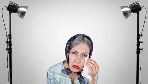 Woman in plaid shirt wiping tears from her face under studio lighting setup.