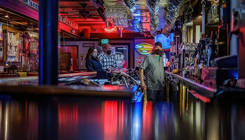 Neon-lit bar interior with red and blue lighting, customers at counter, reflections on wet surface.