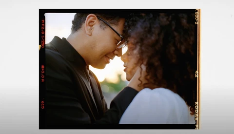 Two people facing each other in close proximity during golden hour, one wearing glasses and a black jacket.