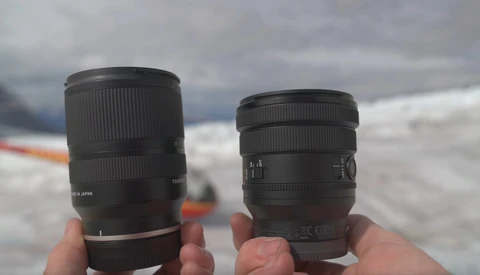 Two telephoto lenses held in hands against a snowy mountain landscape.