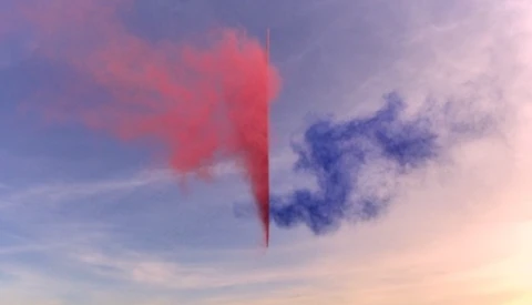 Red and blue smoke clouds dispersing against a pastel sunset sky.
