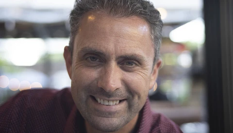 Middle-aged man with gray hair smiling at camera in indoor setting with blurred background.