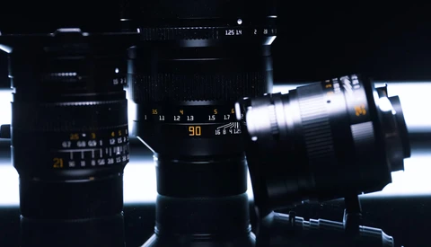 Collection of camera lenses arranged against backlit white background, showing focus rings and aperture markings.