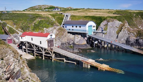 Coastal boathouses and moored vessels nestled against rocky cliffs with turquoise water.