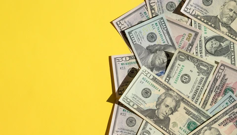Multiple U.S. dollar bills scattered on a bright yellow background.