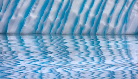 Underwater view of a swimming pool with rippling water surface and blue lane dividers reflecting light.