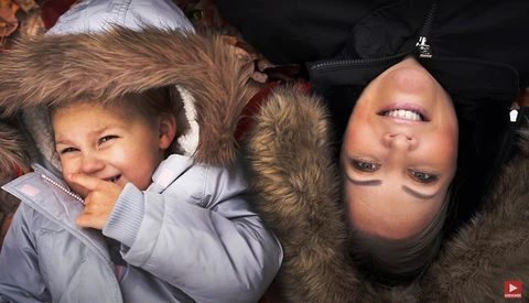 Woman and child lying on their backs, smiling at camera with heads tilted upside down.