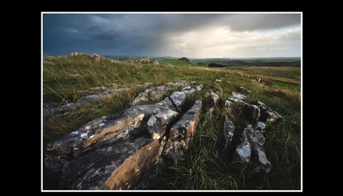 Weathered rock outcrop in grassland with dramatic cloudy sky and distant hills.
