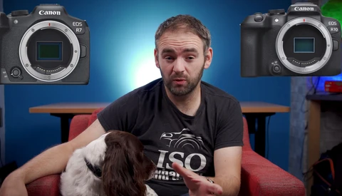 Man holding a brown and white dog, seated between two Canon EOS R mirrorless cameras displayed on a blue backdrop.