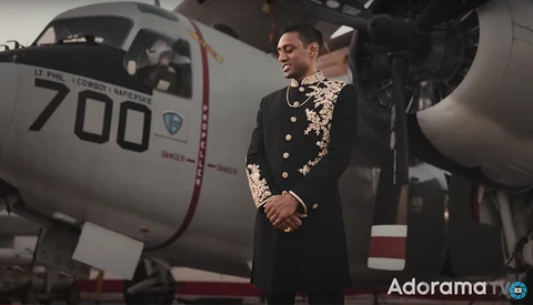 Man in ornate black military dress uniform standing beside aircraft fuselage numbered 700.