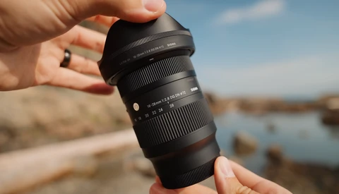 Photographer holding a telephoto zoom lens outdoors with a coastal landscape in the background.