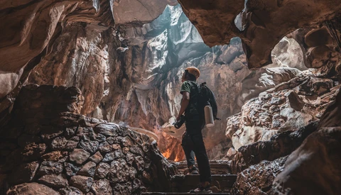 Hiker standing in cave opening overlooking snow-covered mountain valley.