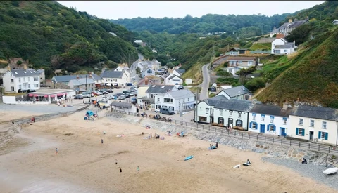 Aerial view of a crowded beach town nestled in green hills with Victorian-era buildings and a sandy shore.