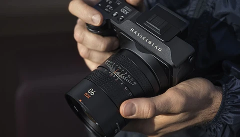 Photographer holding a Hasselblad camera with a Zeiss lens attached.