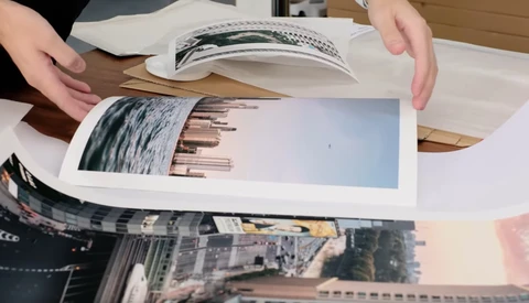 Hands arranging printed photo prints on a wooden table, including landscape and architectural images.