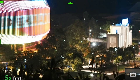 Night cityscape with illuminated modern building and classical structure among trees.