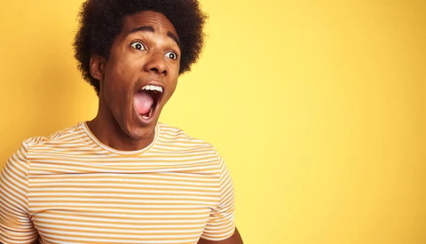 Young man with afro hair sticking out tongue against bright yellow background.