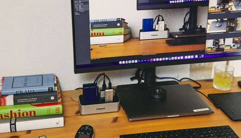 Creative workspace with monitor displaying editing software, desk accessories, and stacked books on wooden surface.