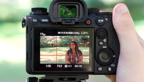 Screenshot showing camera LCD display with live view of woman in red shirt, exposure settings visible at bottom.