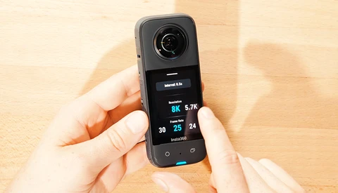 Hands holding a 360-degree camera displaying 8K resolution and 5.7K frame rate specs on its screen.