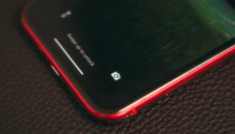 Red smartphone with dark screen on textured fabric surface, showing camera icon and notification indicators.
