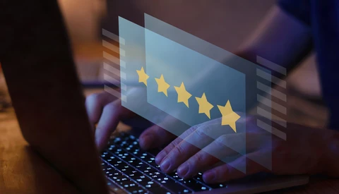 Hands typing on a laptop keyboard with a glowing five-star rating graphic floating above the screen.