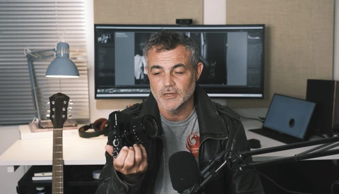 Man in black leather jacket speaking into microphone in home studio setup.