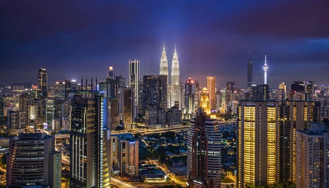Illuminated city skyline at dusk with twin towers and dense high-rise buildings.