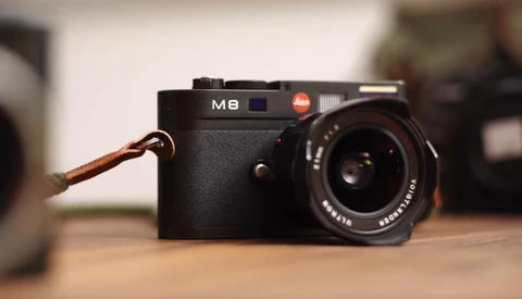 Leica M8 rangefinder camera with leather strap on wooden surface.