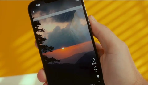 Hand holding smartphone displaying sunset landscape photo with social engagement metrics visible on screen.