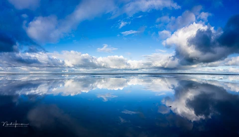 Perfectly mirrored sky and clouds reflected in still water at horizon line.