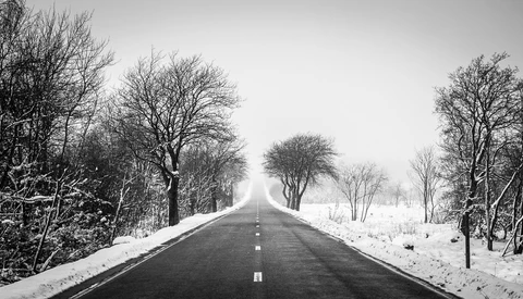 Straight asphalt road stretching toward the horizon, lined with bare trees and snow-covered fields on both sides.