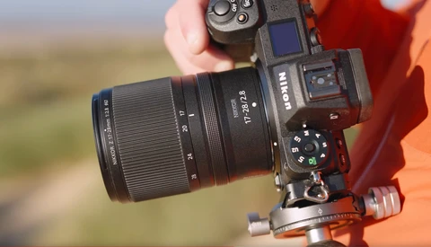 Mirrorless camera with telephoto lens mounted on red gimbal head, held against blurred landscape background.