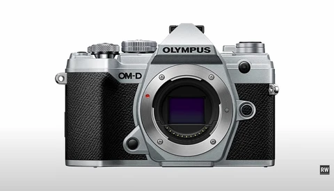 Olympus OM-D mirrorless camera body shown from front, silver and black finish with visible sensor and controls.