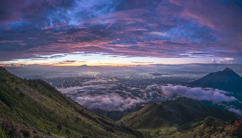 Dramatic dawn landscape with layered mountains and valley fog beneath a purple and pink sky.