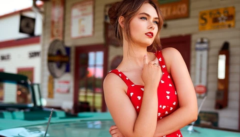 Woman in red polka dot dress posing against billiard table in vintage-style interior.