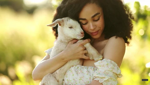 Woman holding a young white goat outdoors in natural daylight.