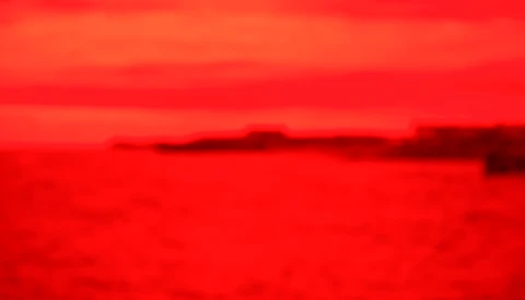 Blurred landscape with red-toned sky and dark landforms along the horizon.