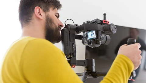 Videographer in yellow shirt operating a cinema camera mounted on a stabilizing rig.