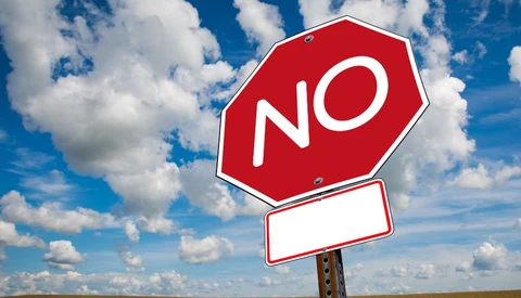 Modified stop sign reading "NO" with blank rectangular sign below, set against blue sky with white clouds.
