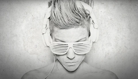 Monochrome portrait of person wearing slotted sunglasses and headphones with shaved undercut hairstyle.