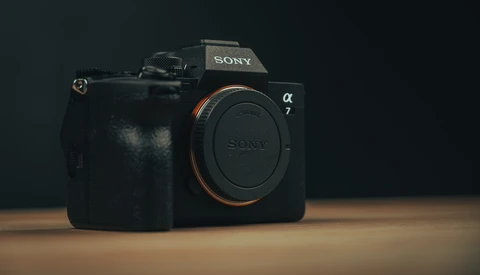 Sony a7 mirrorless camera body displayed against dark background on wooden surface.