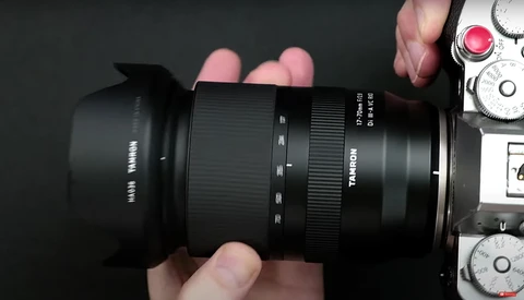 Hands holding a black telephoto lens with a lens hood attached, mounted on a camera body.