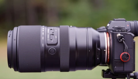 Telephoto lens mounted on a mirrorless camera body with blurred green background.