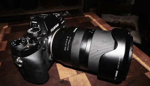 Fujifilm mirrorless camera with attached telephoto lens on wooden surface.