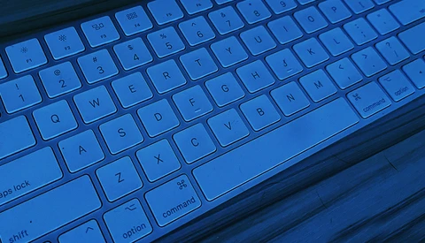 Backlit laptop keyboard illuminated in blue with shallow depth of field.