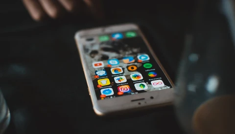 Smartphone with colorful app icons displayed on screen, held at an angle in dim lighting.