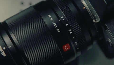 Close-up of a black telephoto lens showing aperture markings and a red depth-of-field indicator button.
