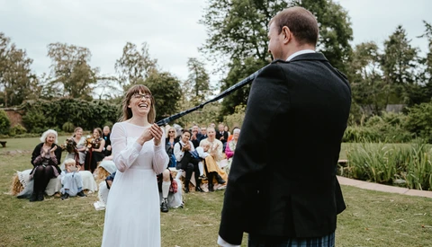 Bride and groom during outdoor wedding ceremony with seated guests in background.