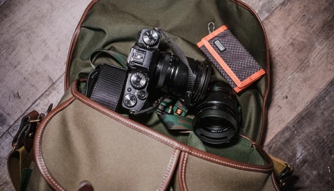 Mirrorless camera with attached lens inside a canvas and leather camera bag on a wooden surface.